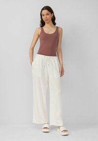 Bruine tanktop met een ronde hals, gecombineerd met witte, losse, strikbare broek en witte platformsandalen. Glad materiaal, casual uitstraling.