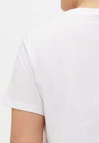 Kortermet hvit t-skjorte, laget av bomull, med rund hals, glatt tekstur, som har et enkelt design uten mønstre eller synlige logoer.