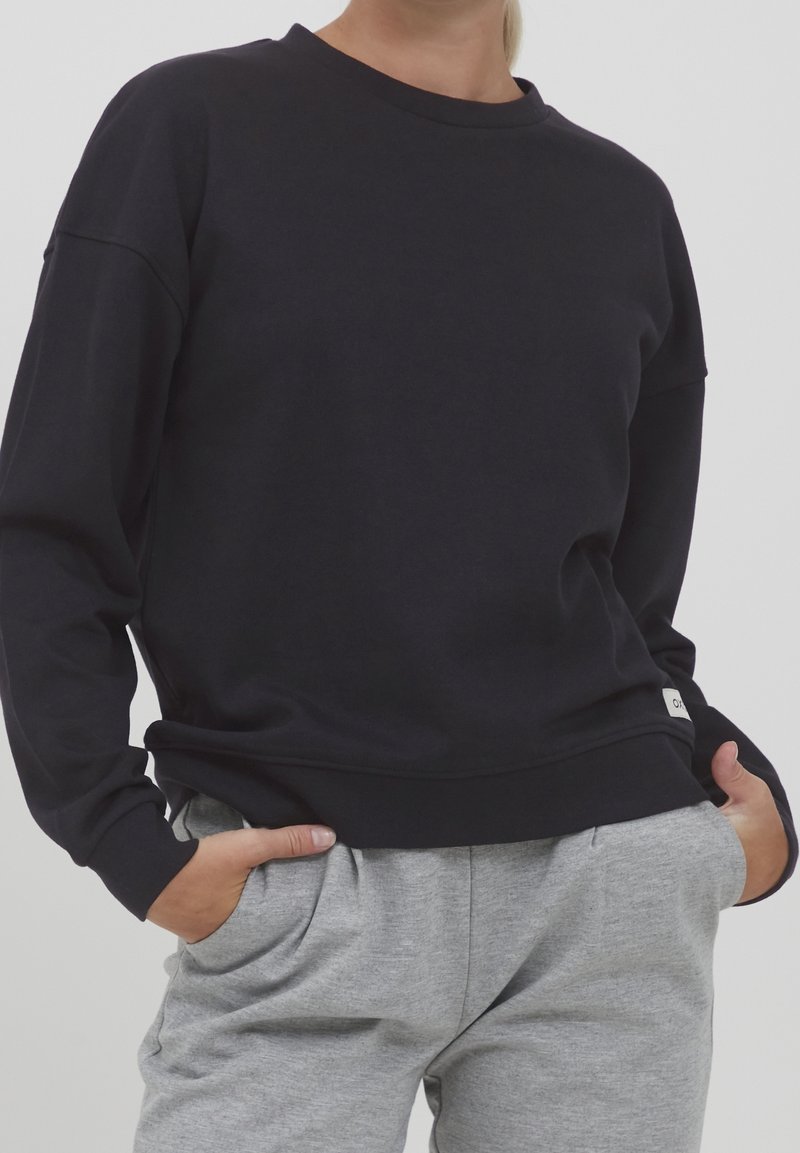 Felpa nera con collo rotondo realizzata in tessuto morbido. Presenta una vestibilità comoda, maniche lunghe e un piccolo marchio vicino all'orlo. Abbinarla a pantaloni grigi.