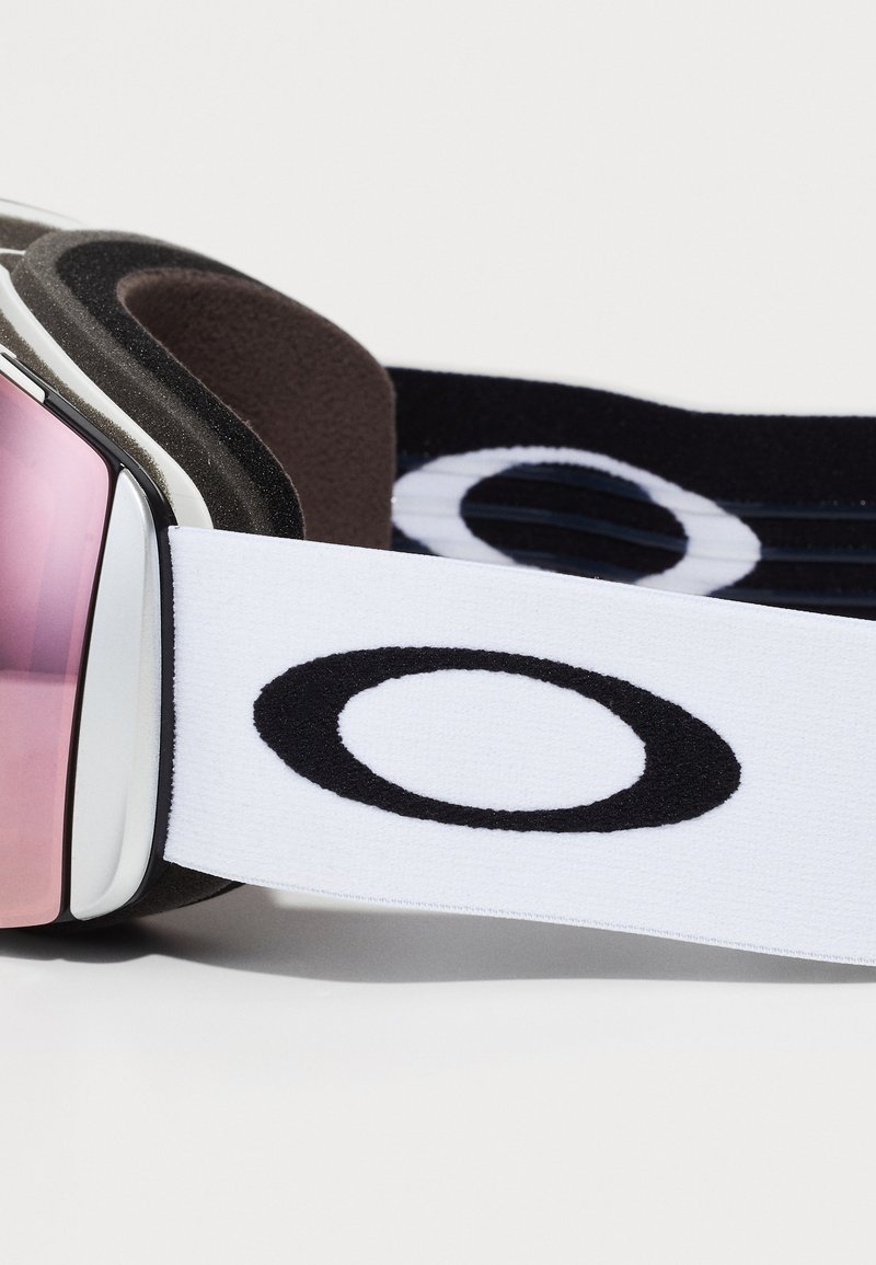 Skibrille mit rosa getöntem Glas, schwarzem Schaumstoffpolster und einem weißen Band mit einem schwarzen runden Logo. Glatte Oberfläche und elegante Kanten.