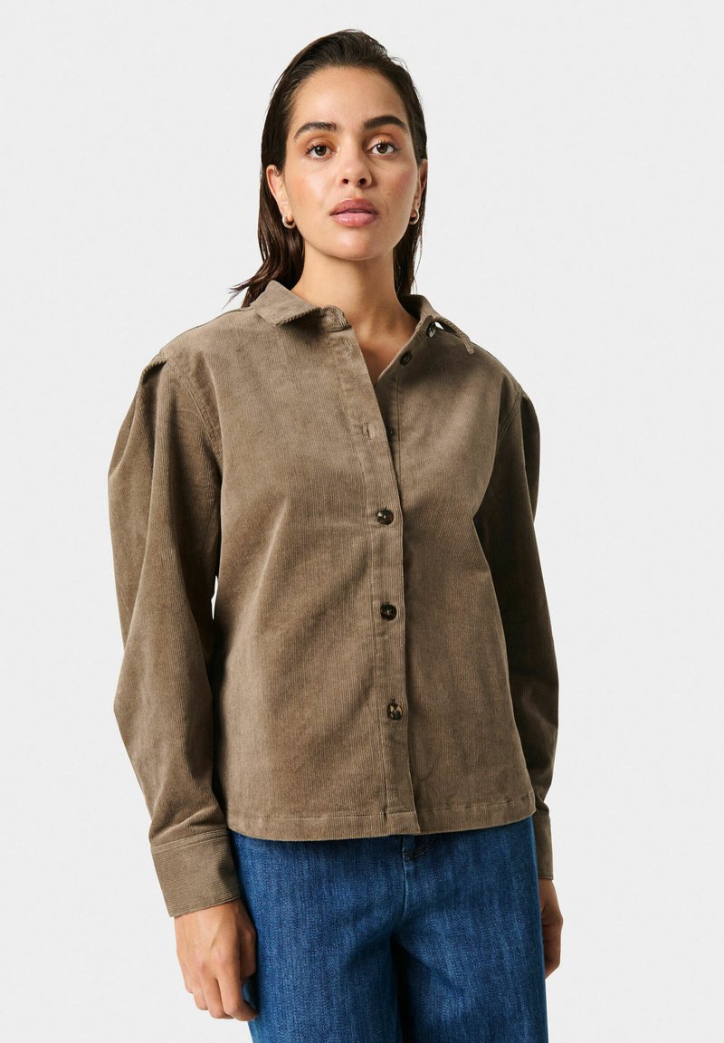 Brun fløjlsskjorte med krave, knaplukning foran og lange ærmer. Har en afslappet pasform og struktureret stof, parret med denimjeans.