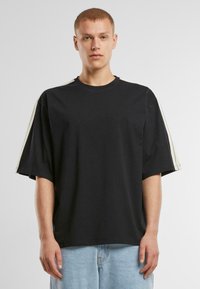 Černé oversize tričko vyrobené z bavlny, s krátkými rukávy a krémovými pruhy. Kolo výstřih a rovný lem. Jednoduchý design.