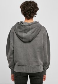 Sweat à capuche gris surdimensionné en tissu doux. Comprend une capuche, des poignets et un ourlet côtelés. Surface légèrement texturée avec une coupe décontractée.