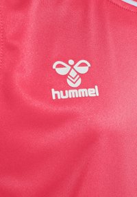 Camiseta deportiva roja hecha de un tejido suave y brillante, que presenta un logo blanco de "hummel" y un diseño gráfico similar a una abeja.