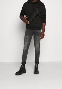 Felpa nera, jeans grigi strappati e stivali Chelsea neri. Accessorio una borsa a tracolla nera con una finitura testurizzata. Abbigliamento casual.