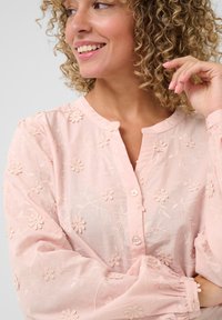 Pink, embroidered blouse with floral patterns, button closure, and puffed sleeves. Lightweight fabric with a soft, textured finish.