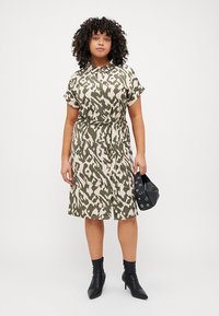 Short-sleeve dress with a green and cream abstract pattern, cinched waist, and knee-length skirt, paired with black ankle boots and a black bag.