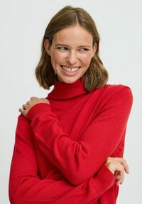 Pulover roșu cu guler înalt, fabricat dintr-un material tricotat moale, având manșete și guler cu nervuri, cu un design ajustat și o textură netedă.