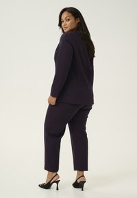 Chaqueta y pantalones de traje morados, hechos de un tejido texturizado. Combinados con tacones negros de punta abierta, que exhiben una silueta elegante.