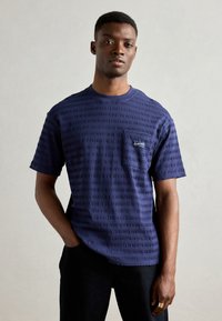 T-shirt bleu marine à manches courtes avec des rayures horizontales texturées, col rond et une petite poche poitrine avec un logo brodé.