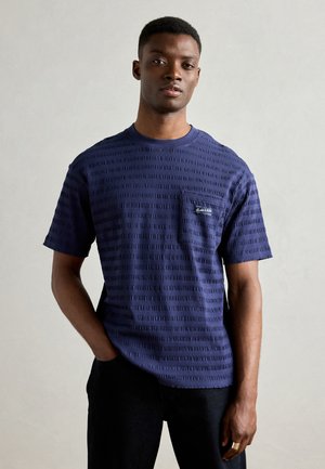 Navy blue short-sleeve t-shirt with textured horizontal stripes, round neckline, and a small chest pocket featuring embroidered branding.