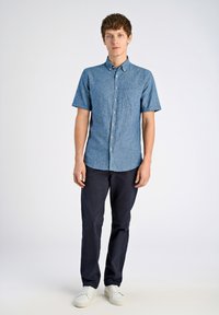 Kortebloemige, lichtblauwe chambray blouse met een button-down kraag en borstzak, gecombineerd met donkerblauwe broek en witte sneakers.