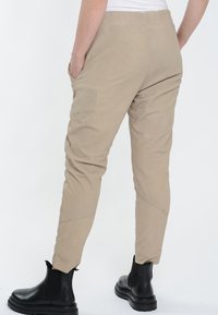 Beige tapse broeken met een soepele textuur, zijzakken en een elastische tailleband, gecombineerd met zwarte enkellaarsjes.