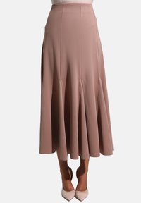 Jupe midi rose en tissu doux, avec un design évasé et des plis pour plus de volume, associée à des escarpins clairs à bouts pointus.