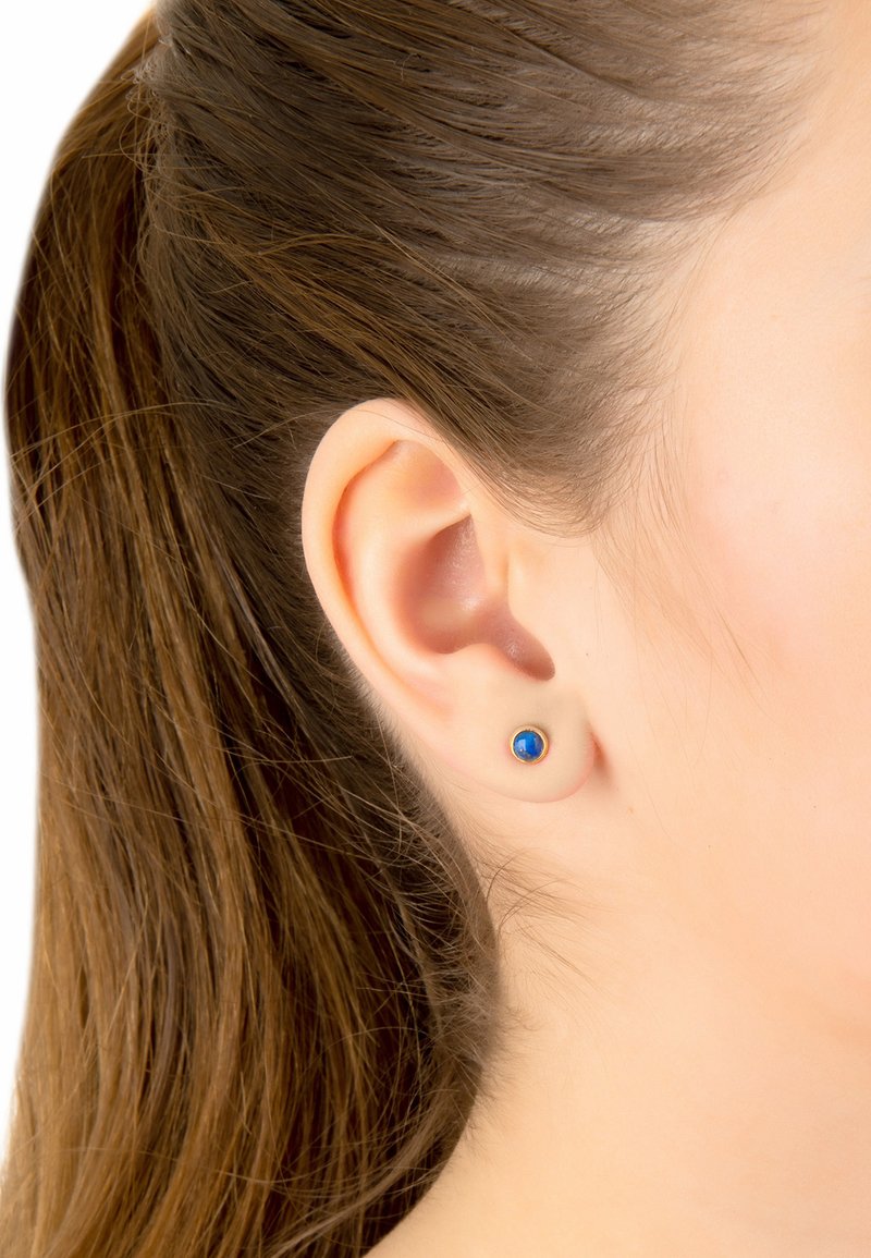 Pendientes de oro en forma de stud con una piedra preciosa azul redonda en el centro. El diseño es simple, con un acabado suave y mínimos detalles.
