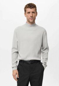 Suéter de tubo de punto acanalado gris claro con mangas largas, combinado con pantalones negros y un cinturón oscuro. Diseño simple y texturizado.