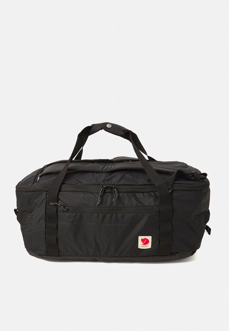 Black nylon duffel bag with zippered compartments and a logo tag. Features two sturdy handles and adjustable shoulder straps. Smooth texture.
