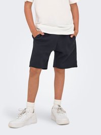 Black cotton shorts with two side pockets, paired with a plain white t-shirt. White sneakers and ribbed crew socks complete the outfit.