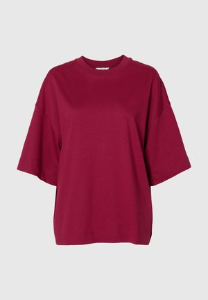 T-shirt à manches courtes, col rond, coupe ample, de couleur bordeaux unie sur un fond gris clair uni.