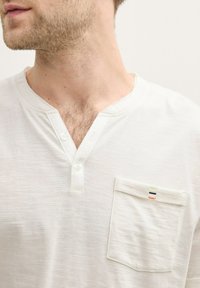 Witte henley-shirt van zachte stof, met een knoopsluiting, een enkele borstzak met veelkleurige stikselaccenten.