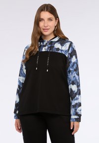 Felpa nera con cappuccio e maniche a fantasia astratta blu e bianca. Presenta lacci decorativi e un'abbottonatura sul collo.