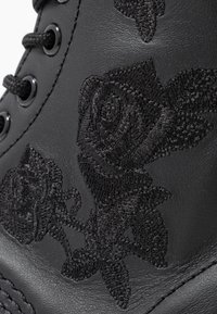 Černé kožené kotníkové boty s vyraženými černými růžovými vzory, kulatými tkaničkami a černými kovovými očky. Hladký povrch a elegantní design.