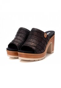 Sandalias de plataforma trenzadas en negro, con punta abierta, que cuentan con un grueso tacón de color tostado y una parte superior texturizada, adornadas con una pequeña etiqueta de logo.