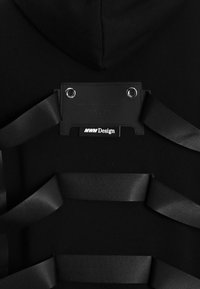 Sudadera negra con un parche de cuero rectangular que muestra "MWM Design", con cintas de satén negras entrelazadas a través de ojales.