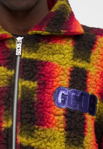 Fleecinė užtrauktuko striukė su spalvinga raštuota patikra raudona, geltona ir žalia spalvomis, su blizgiu "GCDS" logo ant krūtinės.