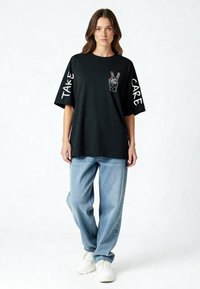 Svart överstor t-shirt med grafisk fredssymbol och texten "TAKE" och "CARE" på ärmarna. Matchas med ljusblå baggy jeans och vita sneakers.