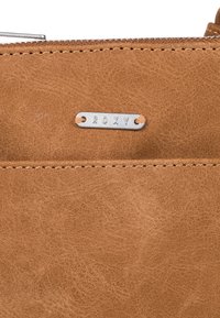 Brun konstläderplånbok med synlig textur, som har en silver Roxy-logotyp och kontrasterande sömmar längs kanterna.