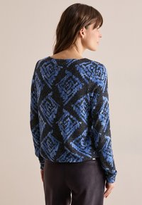 Schwarzer und blauer Pullover mit Rautenmuster, langen Ärmeln und Rundhalsausschnitt. Weiche Textur, mit einem kleinen Knopfdetail am Rücken.