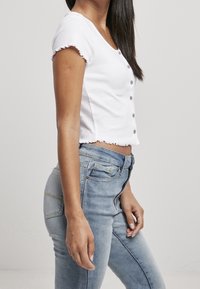 Vit kort topp med korta volangärmar, femknappsstängning, tillsammans med ljusblå högmidjade jeans med fickor.