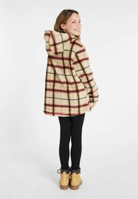 Beige, orange und schwarze karierte Jacke mit Kapuze, aus weichem Stoff gefertigt. Hat eine lockere Passform und eine große Kapuze. Kombiniert mit schwarzen Leggings und braunen Stiefeln.
