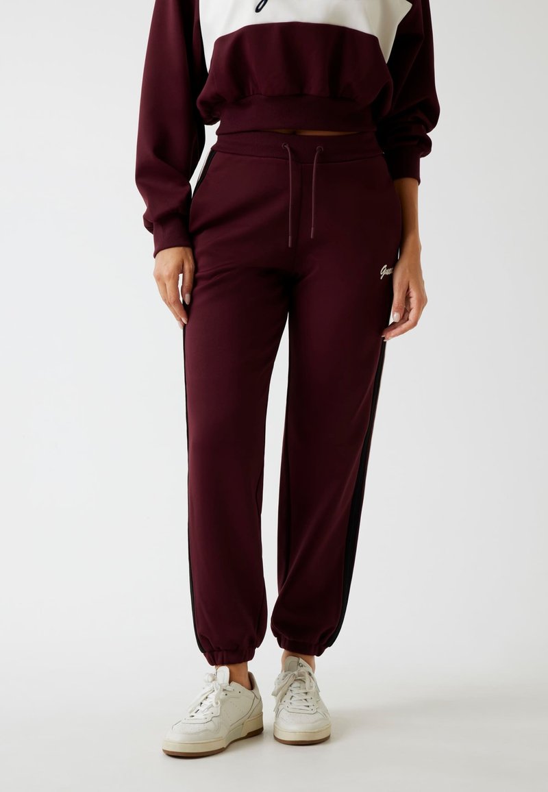 Bordeaux joggers met zwarte zijkanten, elastische boorden en een trekkoord in de taille. Gecombineerd met witte sneakers en een bijpassend bovenstuk.