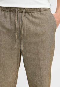 Beige joggebukser laget av et teksturert stoff, med en avslappet passform, sidelommer og en subtil glans.