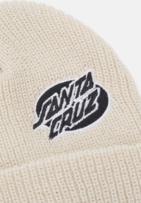 Cream knitted beanie with a folded cuff, featuring a black embroidered "Santa Cruz" logo on a white background. Textured fabric pattern.