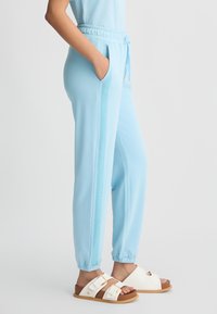Pantaloni jogger azzurri chiari con una striscia laterale texturizzata, vita elastica e polsini elastici, abbinati a sandali bianchi con due fibbie.