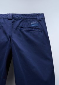 Pantalones azul marino con trabillas para cinturón, bolsillo trasero de ojal y una parche rectangular cosido con el logo "NAPA PIRI".