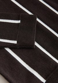 Ciemnobrązowy sweter z poziomymi białymi paskami, ściągaczami przy mankietach i miękką teksturą, podkreślający swój dziany materiał i wzór.