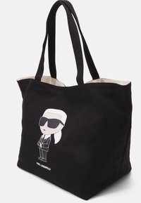 Black canvas tote bag featuring a cartoon character graphic wearing sunglasses. Interior lined in beige, with two sturdy handles.