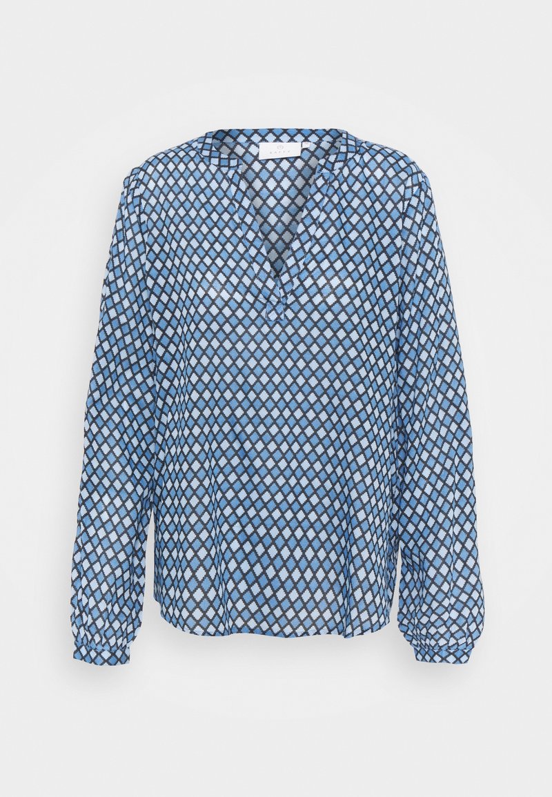 Blouse bleue à manches longues avec motif losanges noir et blanc, col en V et poignets froncés.