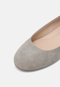 Chaussure plate gris clair avec bout arrondi et dessus en daim lisse, dévoilant une semelle intérieure en cuir beige cousue.