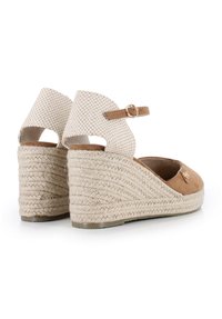 Cuñas de esparto de ante color tostado con una correa de tobillo tejida en crema, punta cerrada y tacón envuelto en yute texturizado. Detalle de hebilla ajustable.