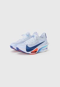 Lys blå strikkede sneakers med en marineblå swoosh, tekstureret øverste og en gradient sål med orange og blå accenter.