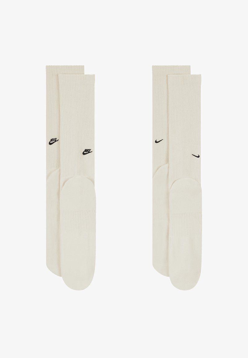 Kreminiu raštuotų iki kelių kojinių su juodais Nike logotipo akcentais išorėje. Minkšta tekstūra ir klasikinis sportinis dizainas.