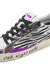 Sneaker con strisce zebra in bianco e nero, dettagli in argento metallico, lacci neri, particolari in glitter viola e testo scritto a mano sulla suola.