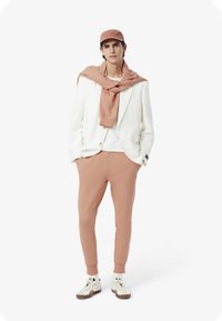 Vit blazer, rosa sweatshirt hängande runt halsen, rosa joggers och en rosa keps. Sneakers med vita och gröna accenter. Enkel, modern design.