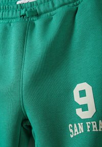 Zaļi kokvilnas sporta bikses ar teksturētu audumu, aukliņu jostasvietu un baltu aplikāciju ar numuru "9" un "SAN FRAN."
