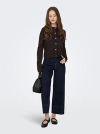 Brauner, geknöpfter Cardigan mit goldenen Akzenten, kombiniert mit dunkelblauen Jeans im Weitbein-Stil, schwarzer Handtasche und schwarzen Ballerinas. Glatter Stoff, lässiges Design.